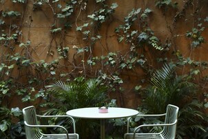 Una mesa redonda con dos sillas en un jardín, con un muro cubierto de hiedra.