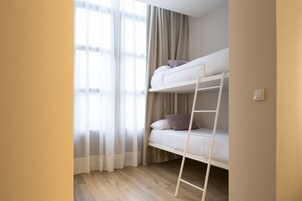 A bunk bed with a ladder, a window with sheer curtains, and a light switch on the wall.