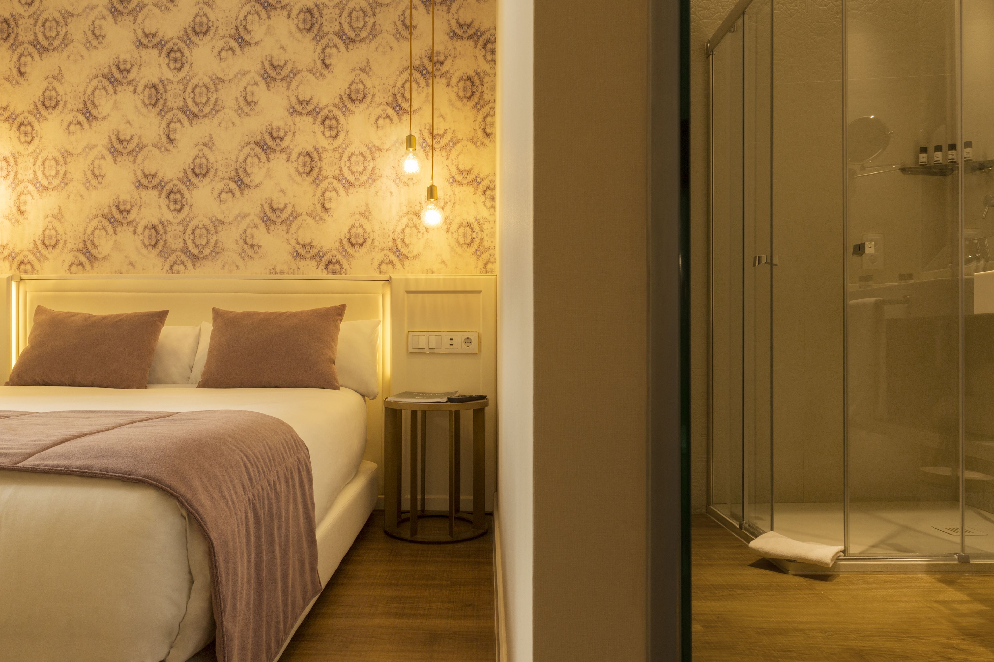 Habitación de hotel con cama, mesita de noche y zona de ducha.