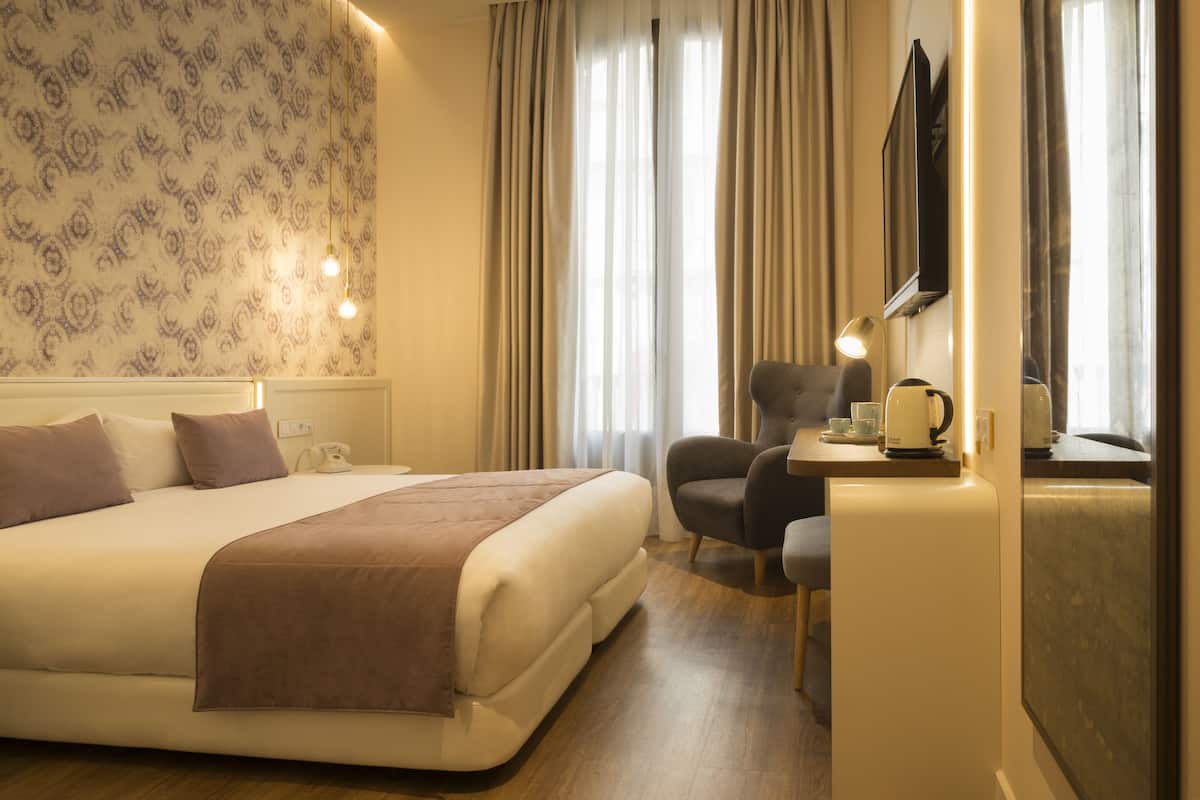 Quarto de hotel com cama, escrivaninha, cadeira, televisão e cortinas.