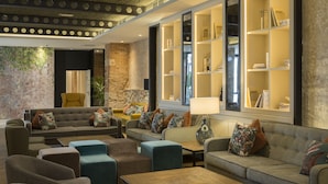 Un área de descanso moderna con sofás, sillones y una mesa de centro. Se observan estanterías con libros y objetos decorativos.