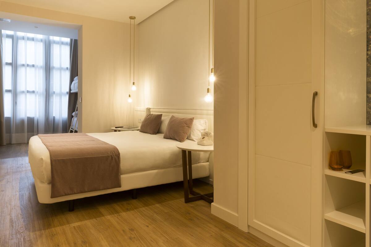 Quarto de hotel com cama, mesa de cabeceira, luminária, guarda-roupa e vista para o exterior.