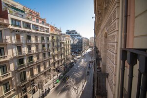 A multi-story building with balconies, a street with vehicles, and a clear sky.