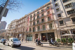 Um edifício de vários andares com um café no andar térreo, uma entrada visível e um céu claro.