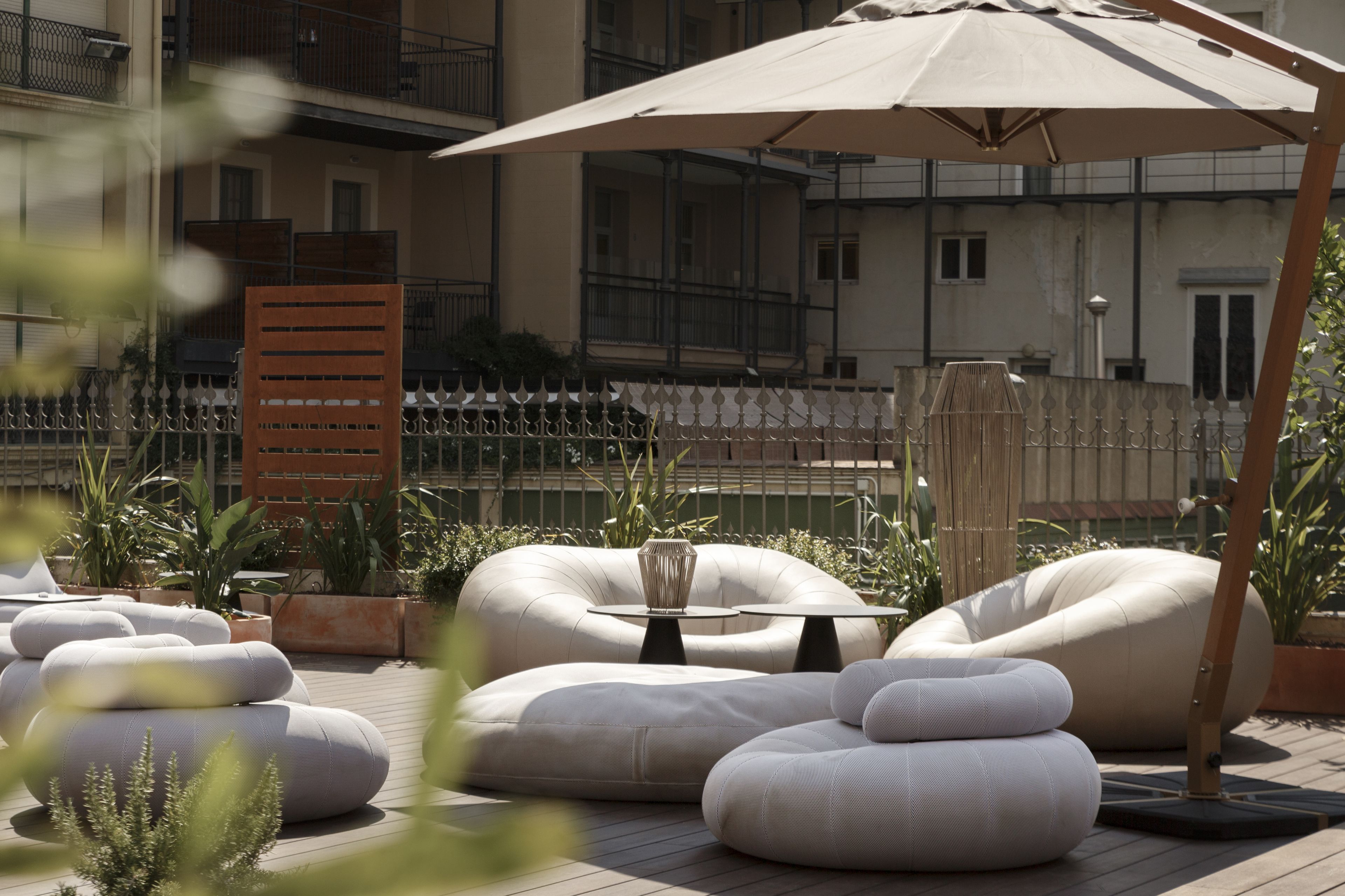 Outdoor seating with a table and umbrella, surrounded by potted plants and a wooden fence.