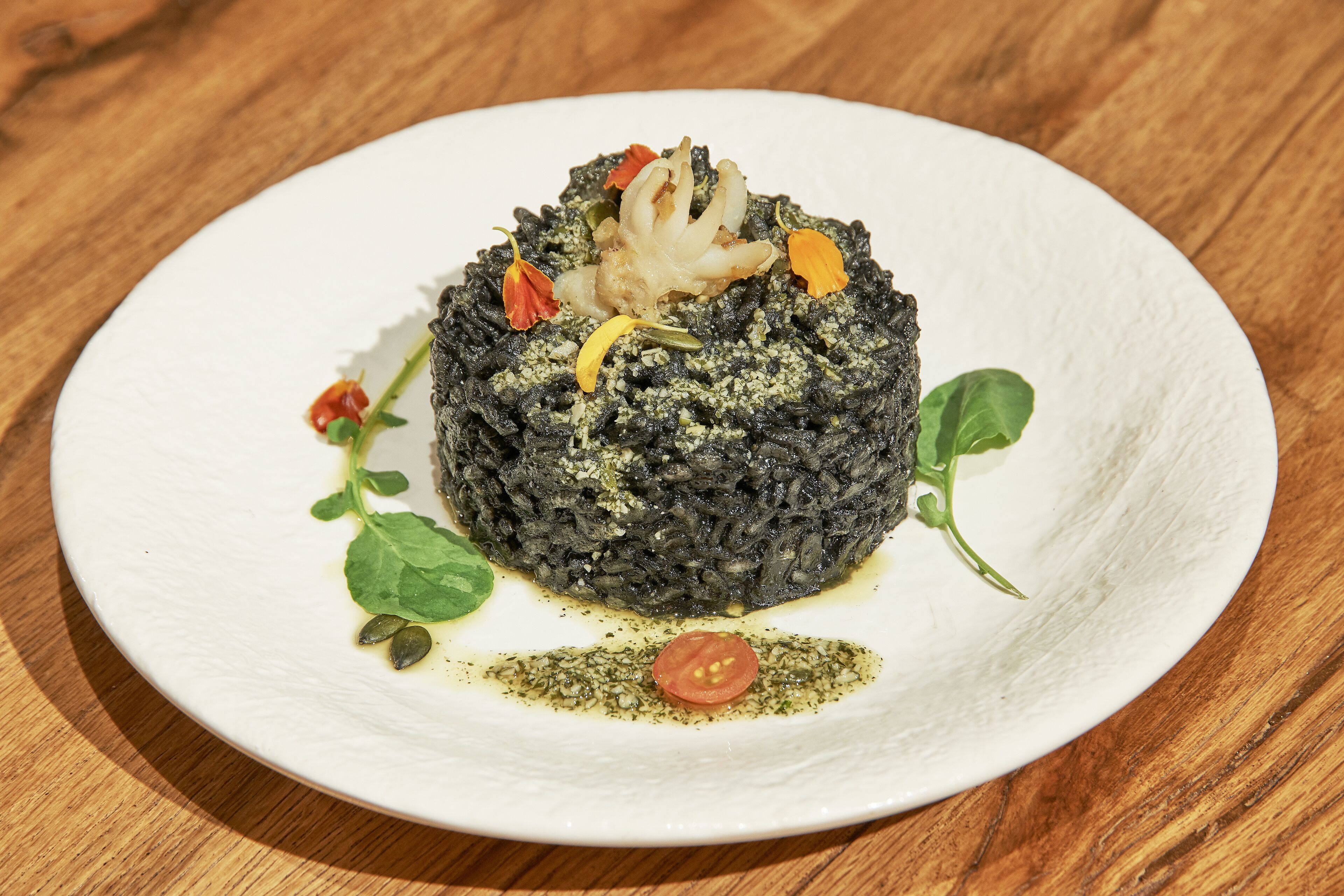 A plate of food with a dark, textured center, garnished with herbs and a small tomato.