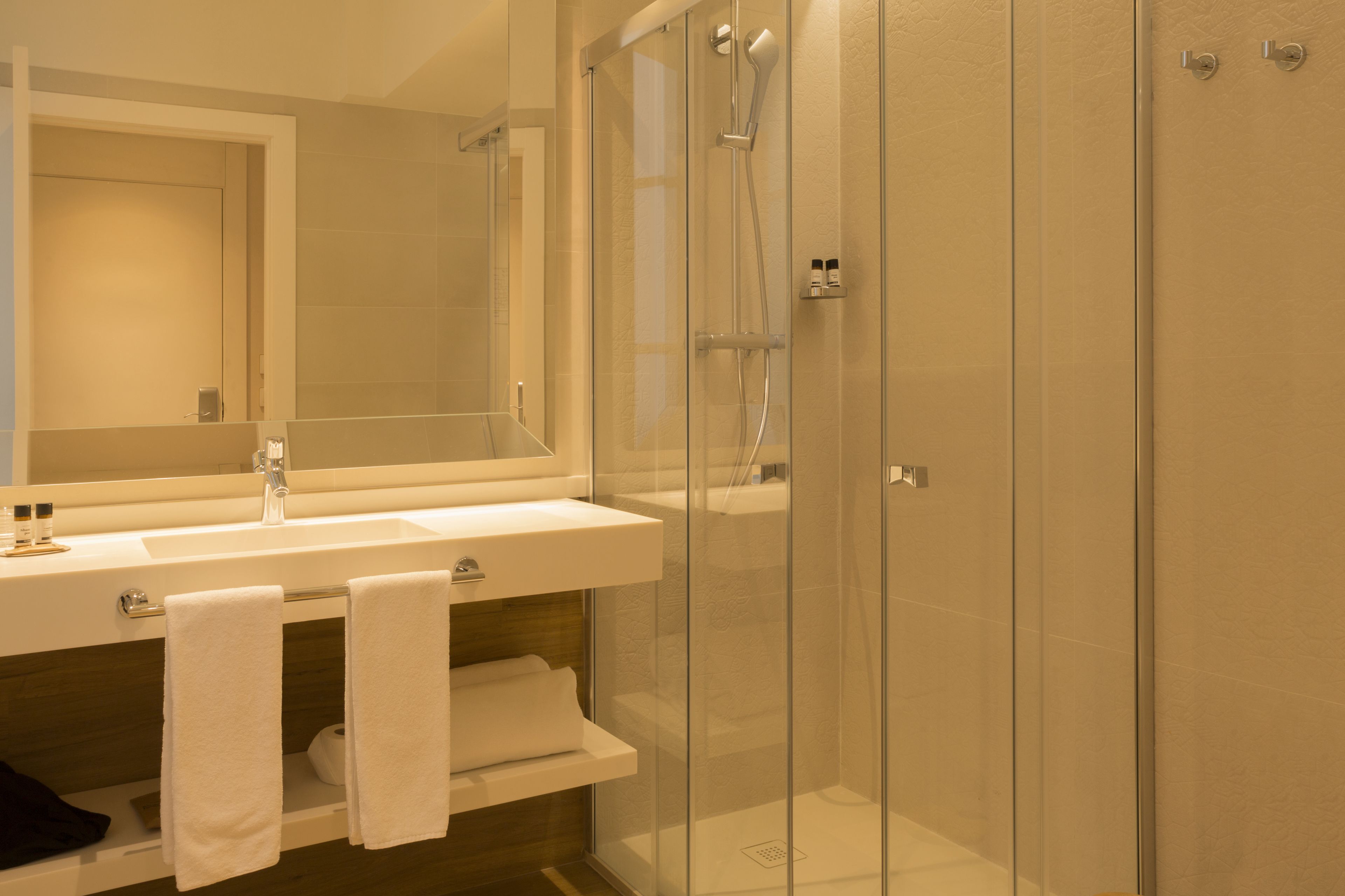 Un baño moderno con ducha de vidrio, un lavabo con espejo y un perchero para toallas.