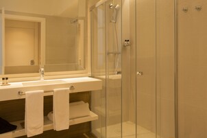 Un baño moderno con ducha de vidrio, un lavabo con espejo y un perchero para toallas.