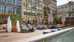 Un área de piscina en la azotea con sillones de descanso, sombrillas y plantas en macetas.