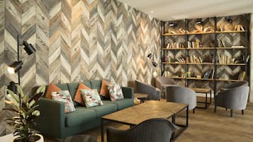 A modern living room with a herringbone-patterned wall, a green sofa with colorful cushions, a wooden coffee table, and a bookshelf filled with books.