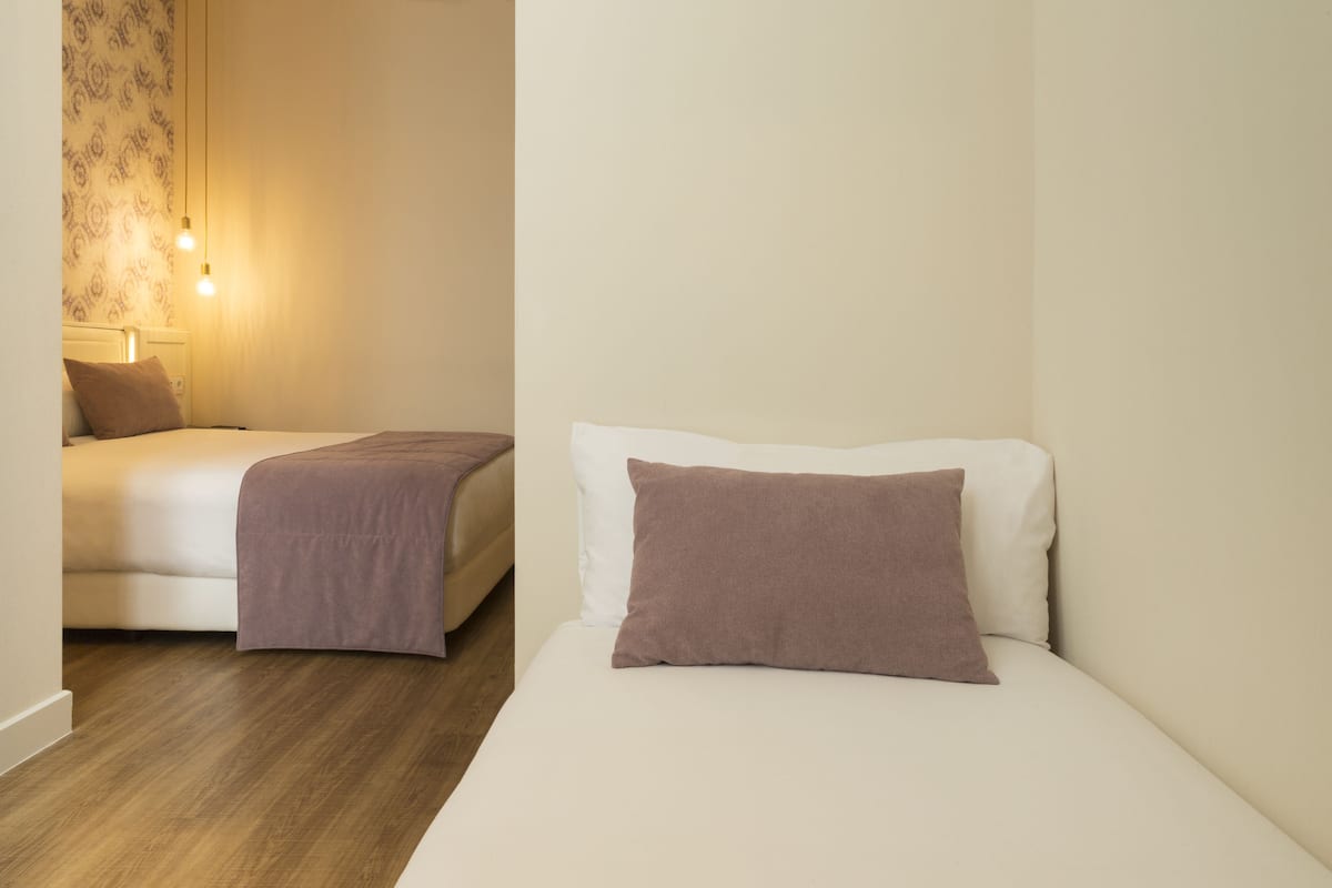 Quarto de hotel com duas camas, piso de madeira e papel de parede estampado.