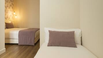 A hotel room with two beds, a wooden floor, and a wall with a patterned wallpaper.