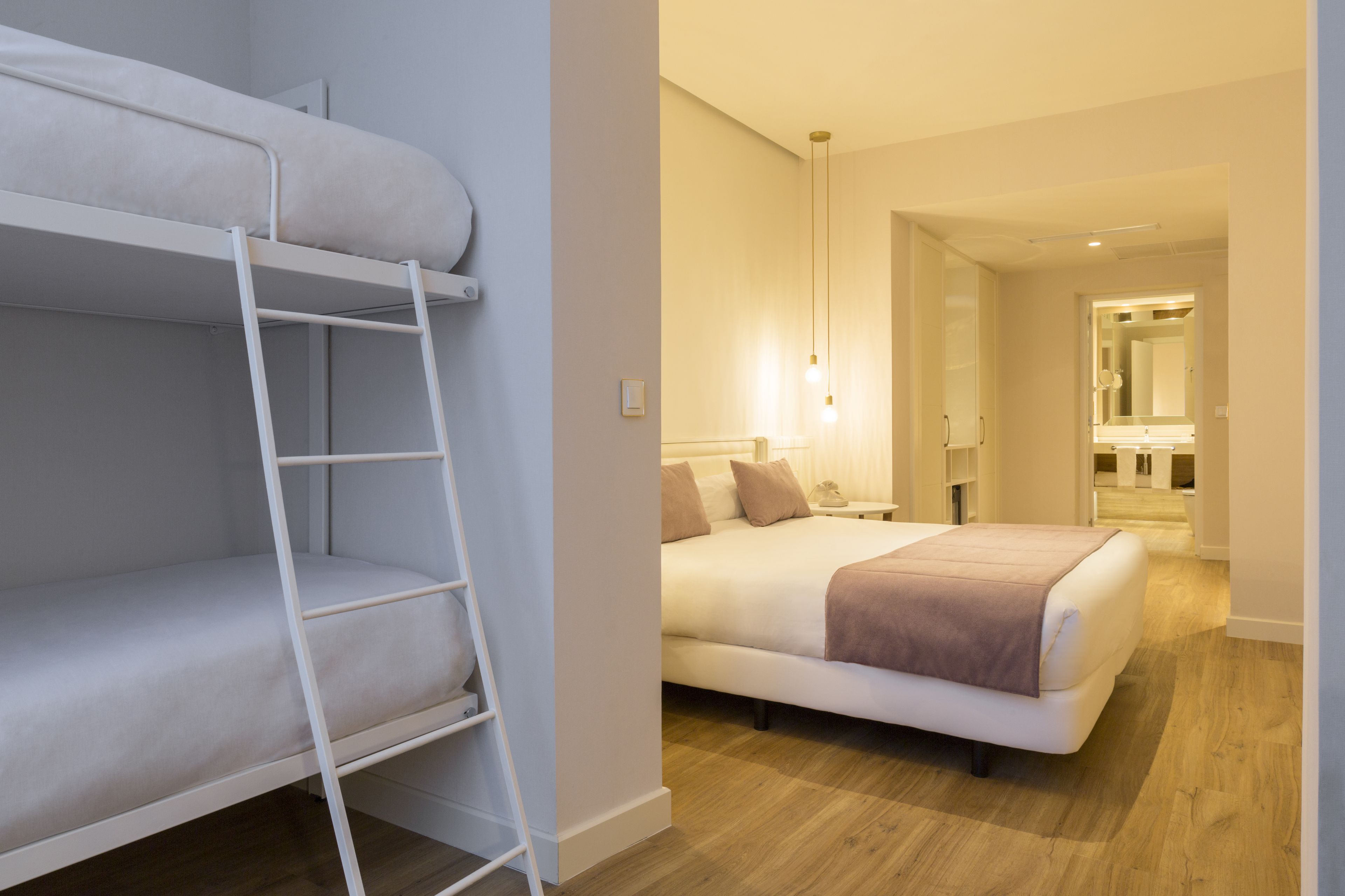Una habitación con una cama nido, una mesita de noche, una lámpara y un espejo.