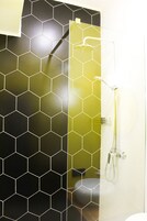 Een badkamer met een betegeling in een honingraatpatroon, een douche en een wastafel.