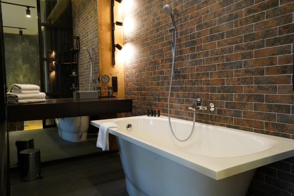 A modern bathroom with a freestanding bathtub, a dark wooden vanity, and a brick wall.