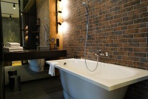 Een moderne badkamer met een vrijstaand bad, een donker houten wastafelmeubel en een bakstenen muur.