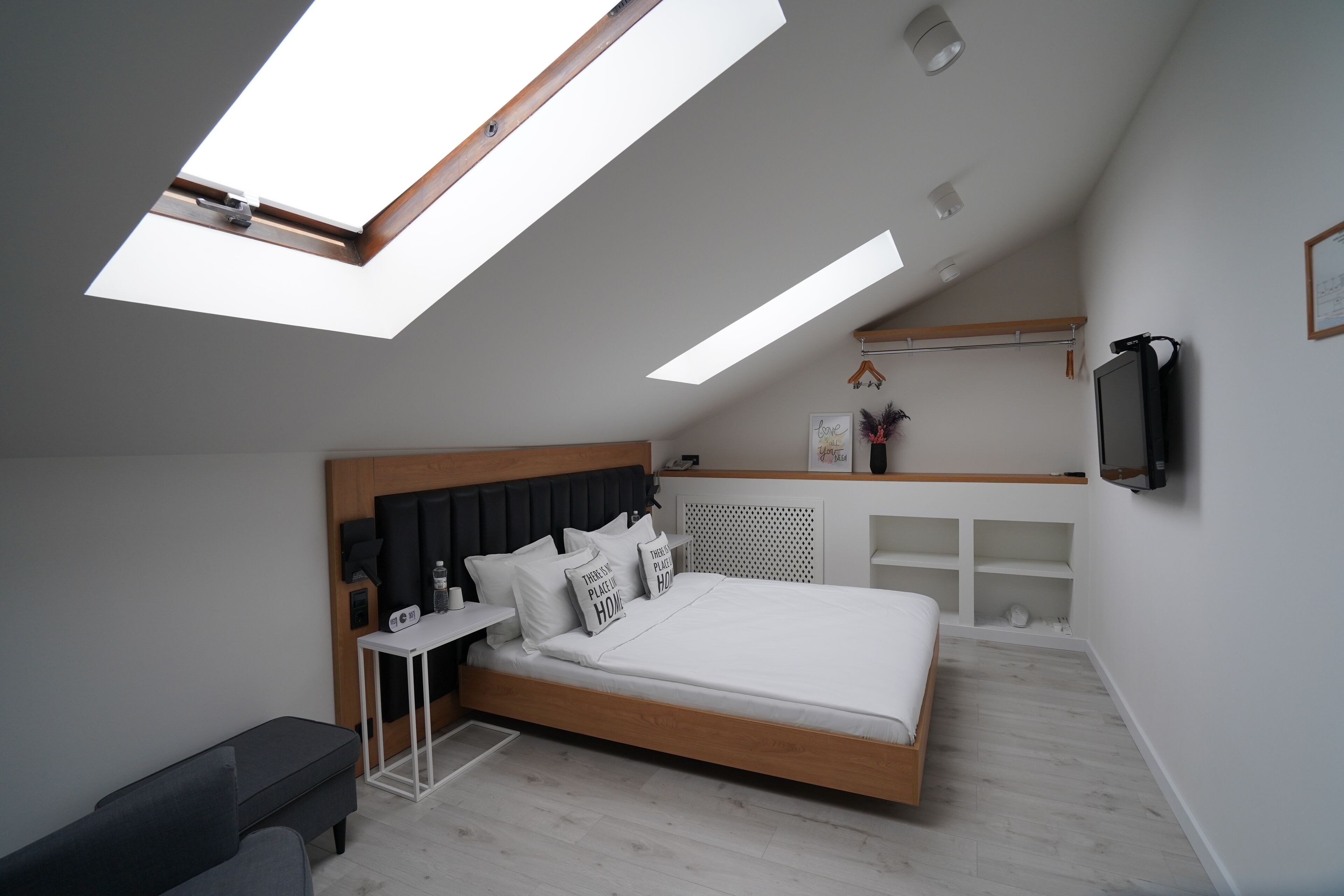 Une chambre moderne avec un puits de lumière, un lit avec une literie blanche, une table de chevet et un téléviseur fixé au mur.