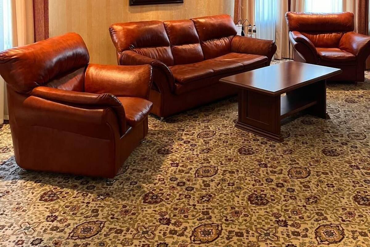 Uma sala de estar espaçosa com um amplo sofá de couro marrom, uma mesa de centro de madeira e um tapete estampado.