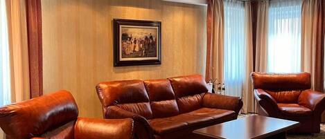 A spacious living room with a large brown leather sofa set, a wooden coffee table, and a patterned carpet.