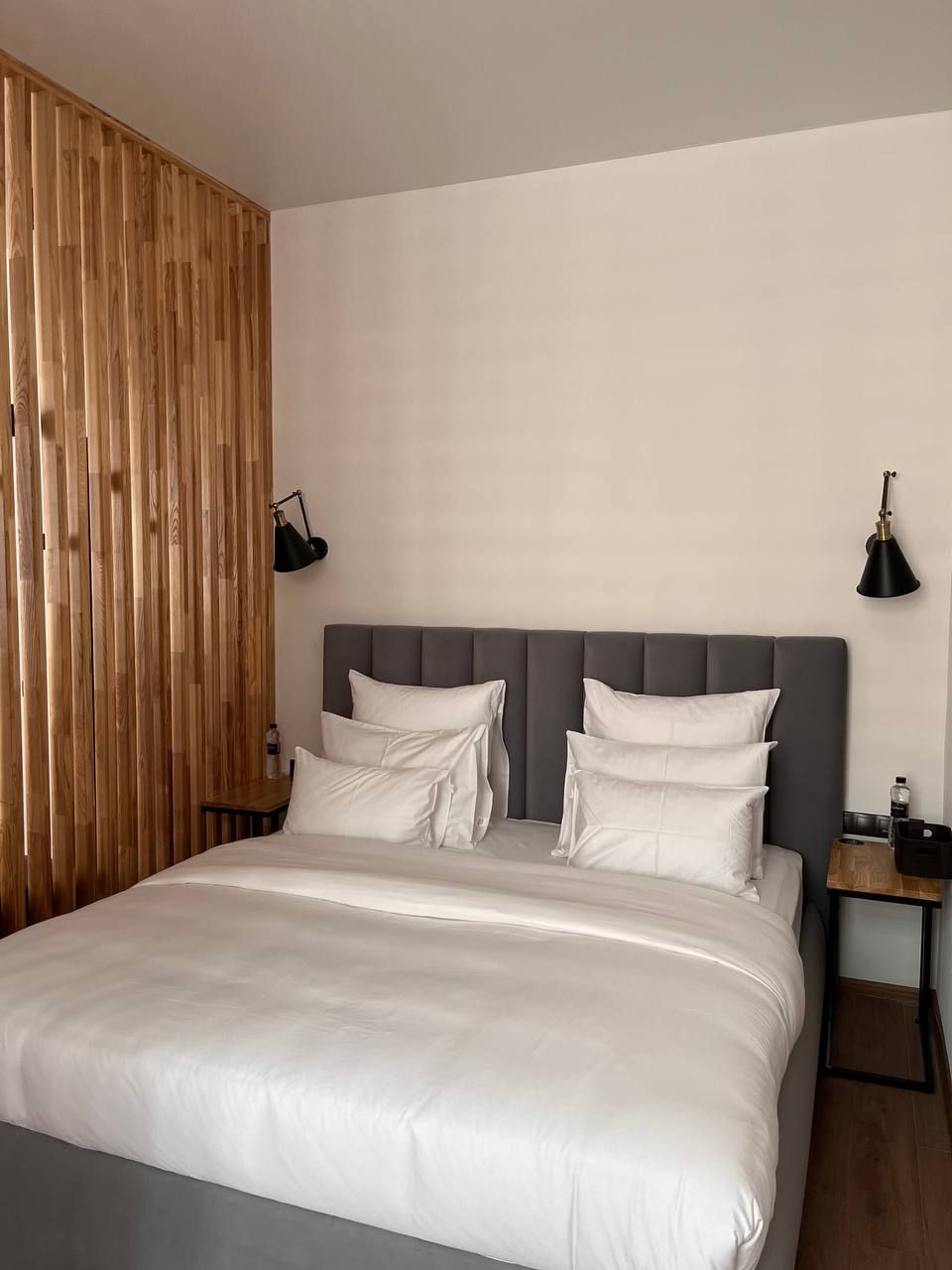 A modern bedroom with a large bed, a wooden partition wall, and two bedside tables with lamps.