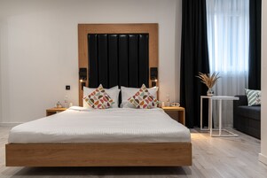 Een moderne slaapkamer met een houten bed, twee nachtkastjes met lampen, een klein bijzettafeltje met een vaas, en een donkere bank.