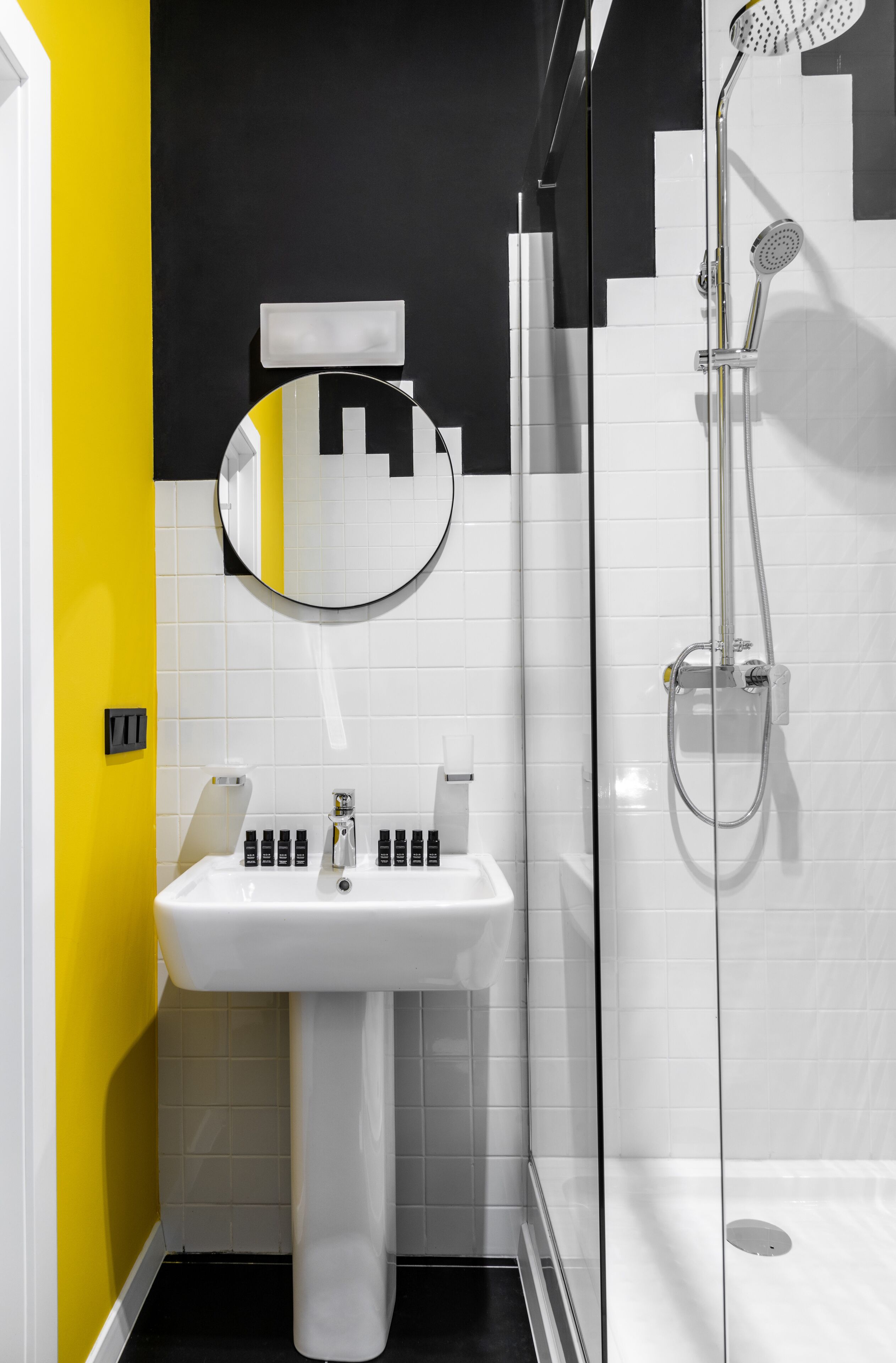 Un baño con lavamanos blanco, espejo y ducha con mampara de vidrio.