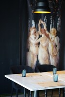 A restaurant with a table set for two, a black chair, and a decorative wall with a painting.