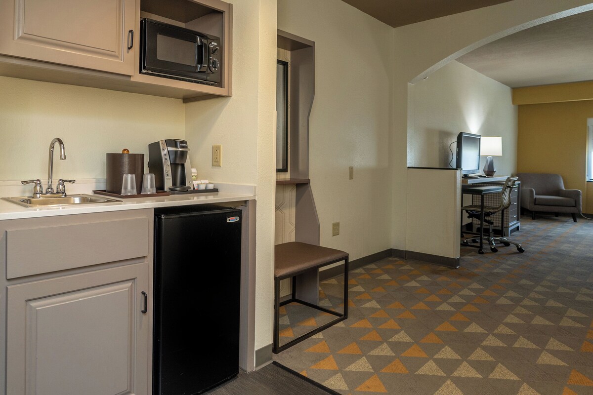 A compact kitchen with a microwave, coffee maker, and refrigerator. A small table and chair are positioned near the kitchen counter.