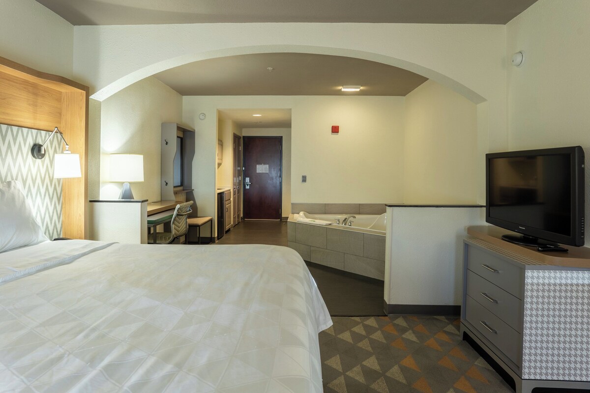 A hotel room with a large bed, a desk with a lamp, a TV, and a bathroom with a bathtub.