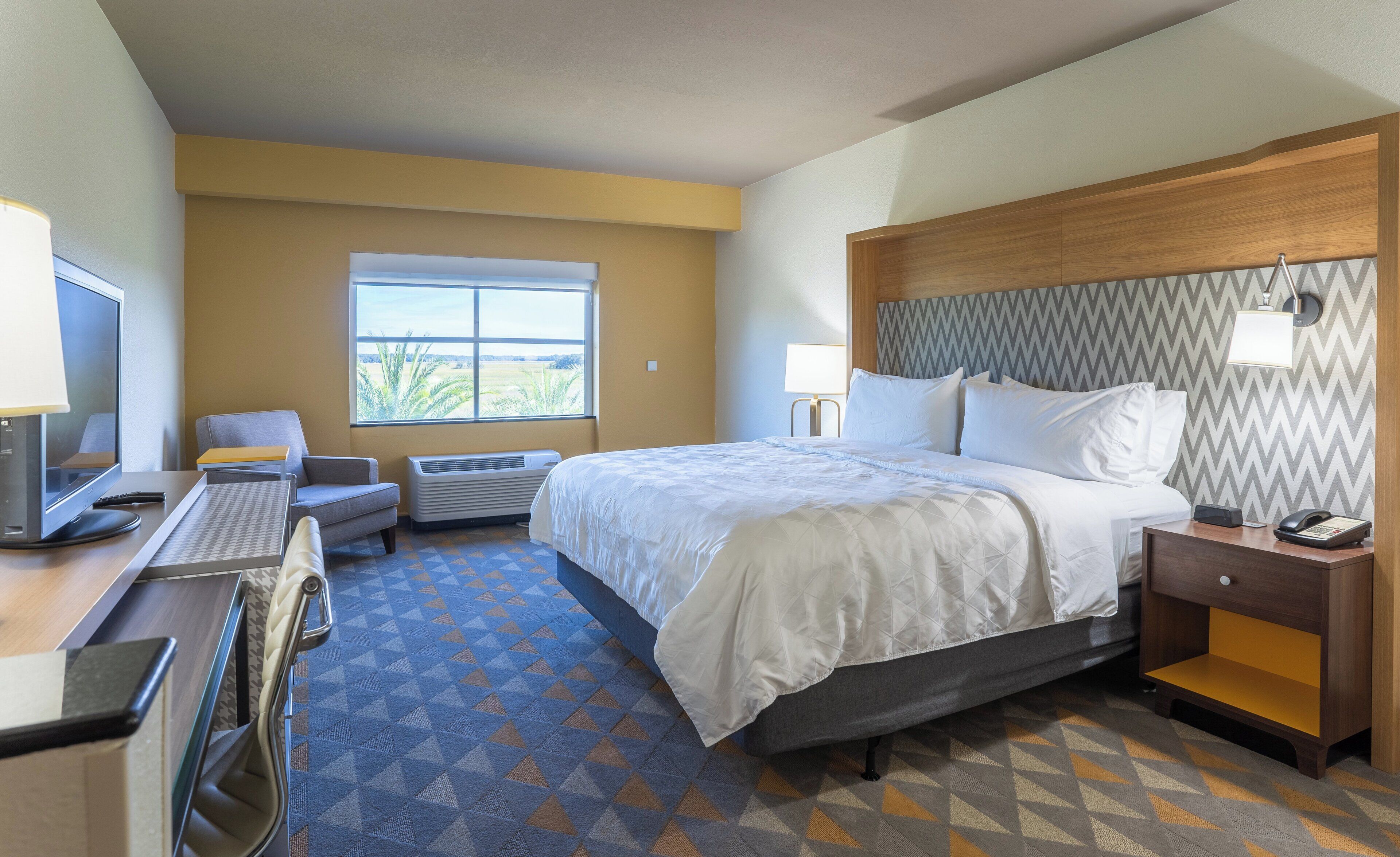 A hotel room with a bed, desk, chair, and a window with a view.