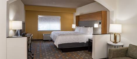 Une chambre d’hôtel avec un lit, deux lampes de chevet, un bureau avec une chaise, un petit canapé et un sol à motifs.