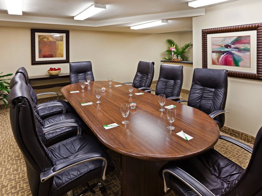 A conference room with a wooden table, black leather chairs, and framed artwork on the walls.
