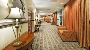 Un pasillo de hotel con alfombra estampada, mostrador de recepción de madera, un sofá y un espejo grande.