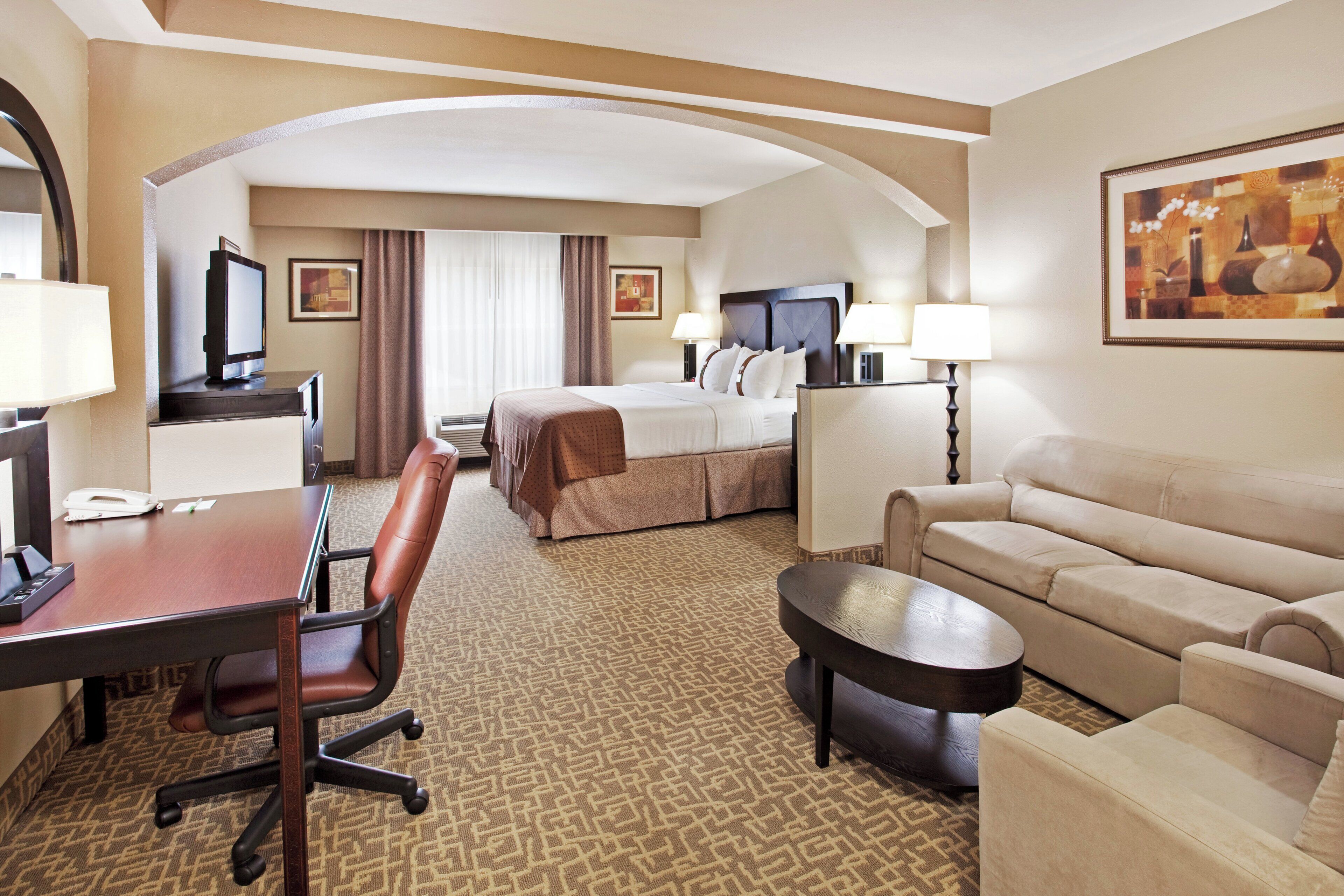 A hotel room with a bed, a desk, a chair, a sofa, and a coffee table.