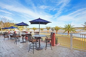 Een terras buiten met tafels, stoelen, parasols en uitzicht op een waterpartij.