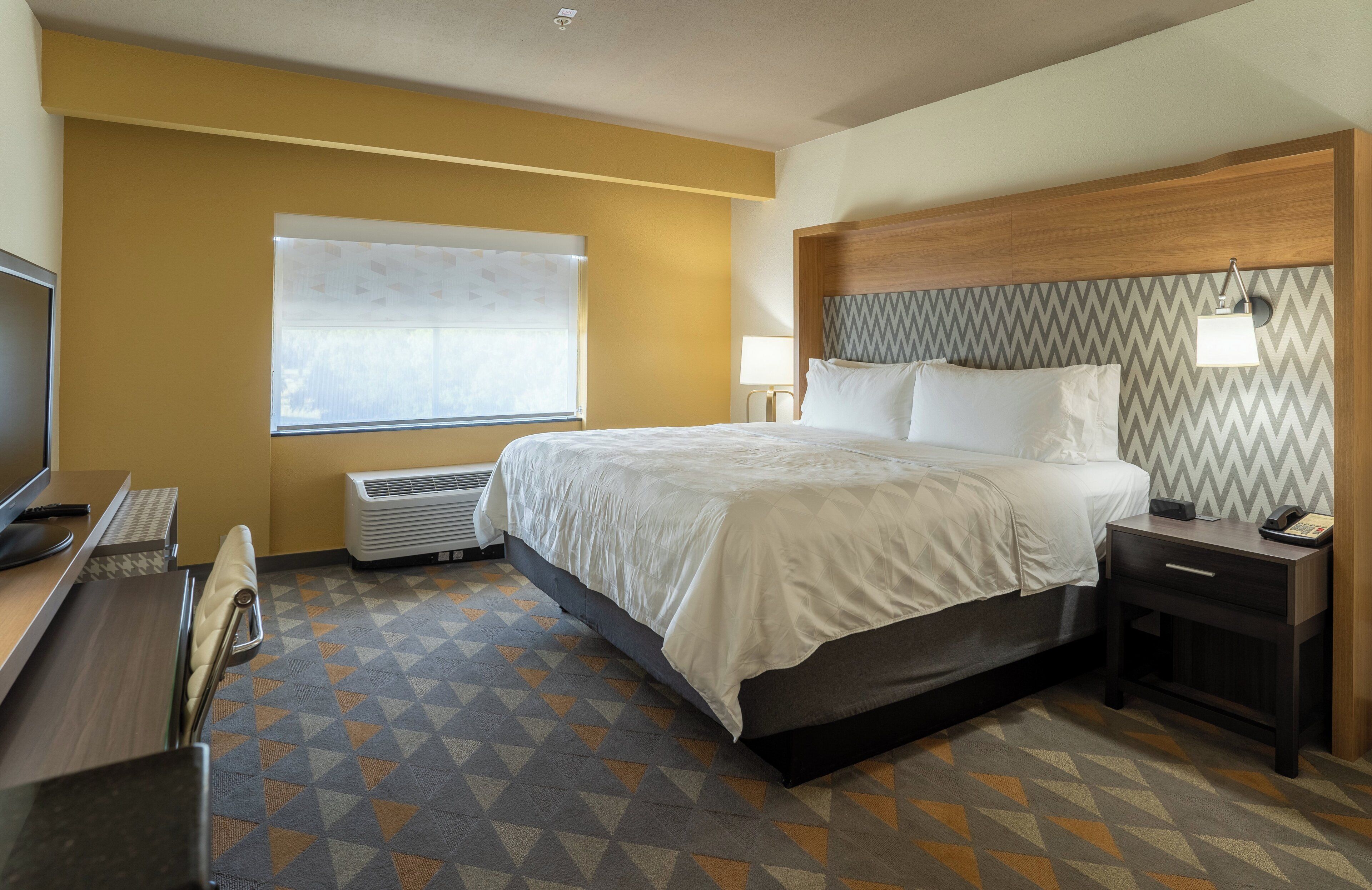 Quarto de hotel com cama, mesa de cabeceira, abajur e escrivaninha com telefone.