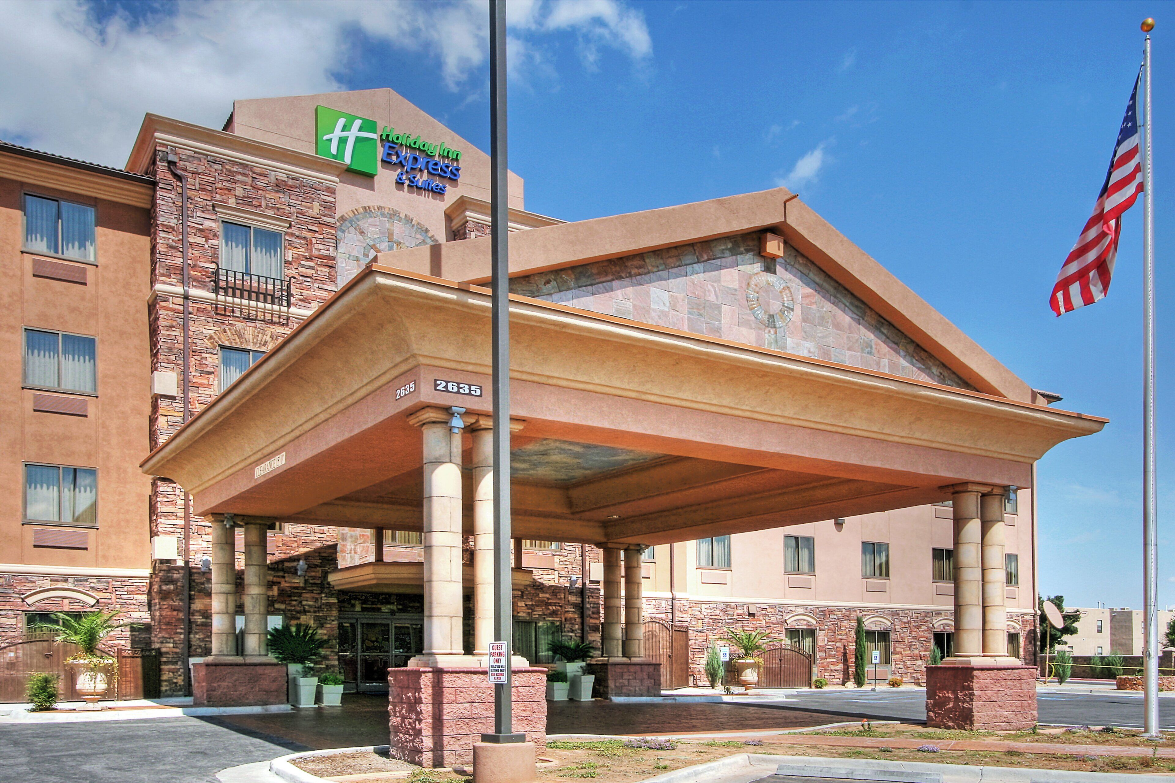 A Holiday Inn Express & Suites hotel with a brick facade, a covered entrance, and an American flag.