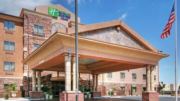 A Holiday Inn Express & Suites hotel with a brick facade, a covered entrance, and an American flag.