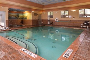 Una piscina interior con agua cristalina, líneas de profundidad marcadas y un cartel de prohibición de clavados.