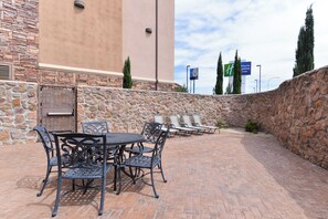 An outdoor patio with a stone wall, a table with chairs, and a view of a motel sign in the background. - Holiday Inn Express Hotel and Suites Las Cruces by IHG (Las Cruces)