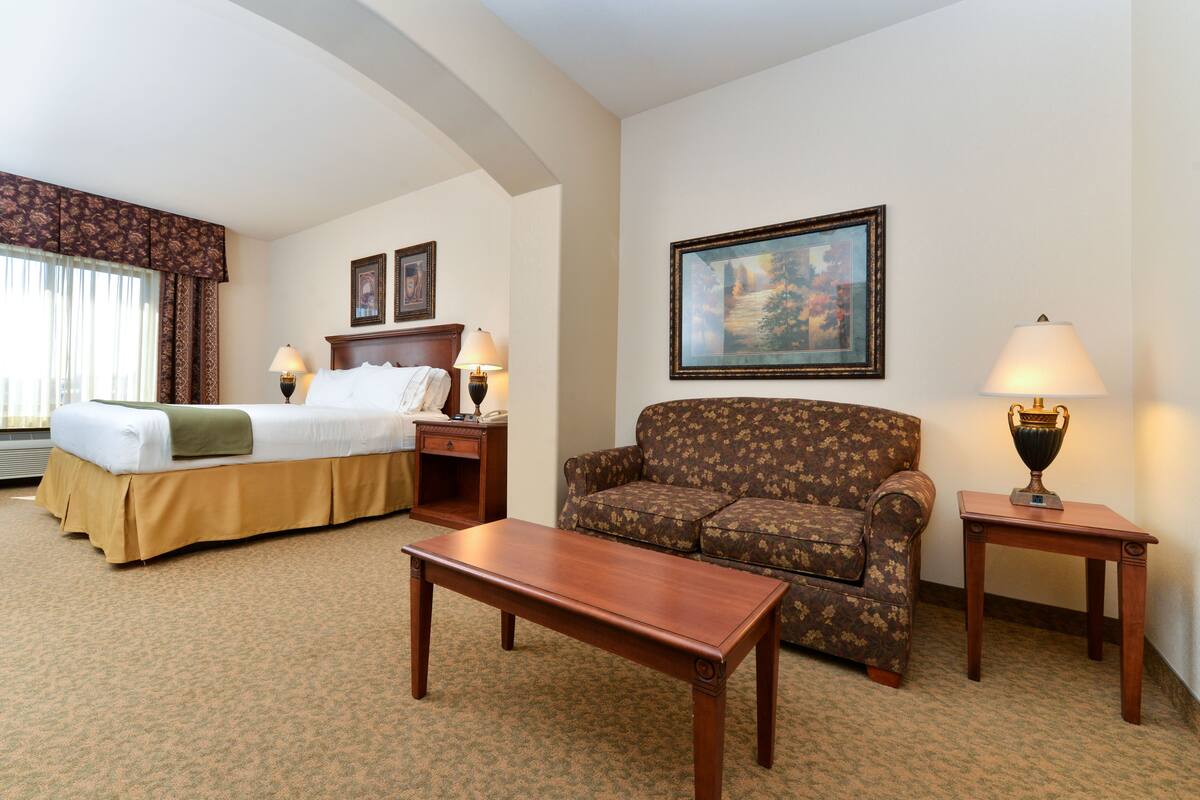 A hotel room with a bed, a sofa, a table, and a lamp.