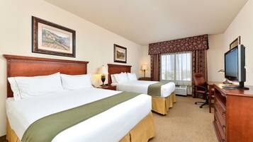 A hotel room with two beds, a desk, a chair, a television, and framed pictures on the wall.