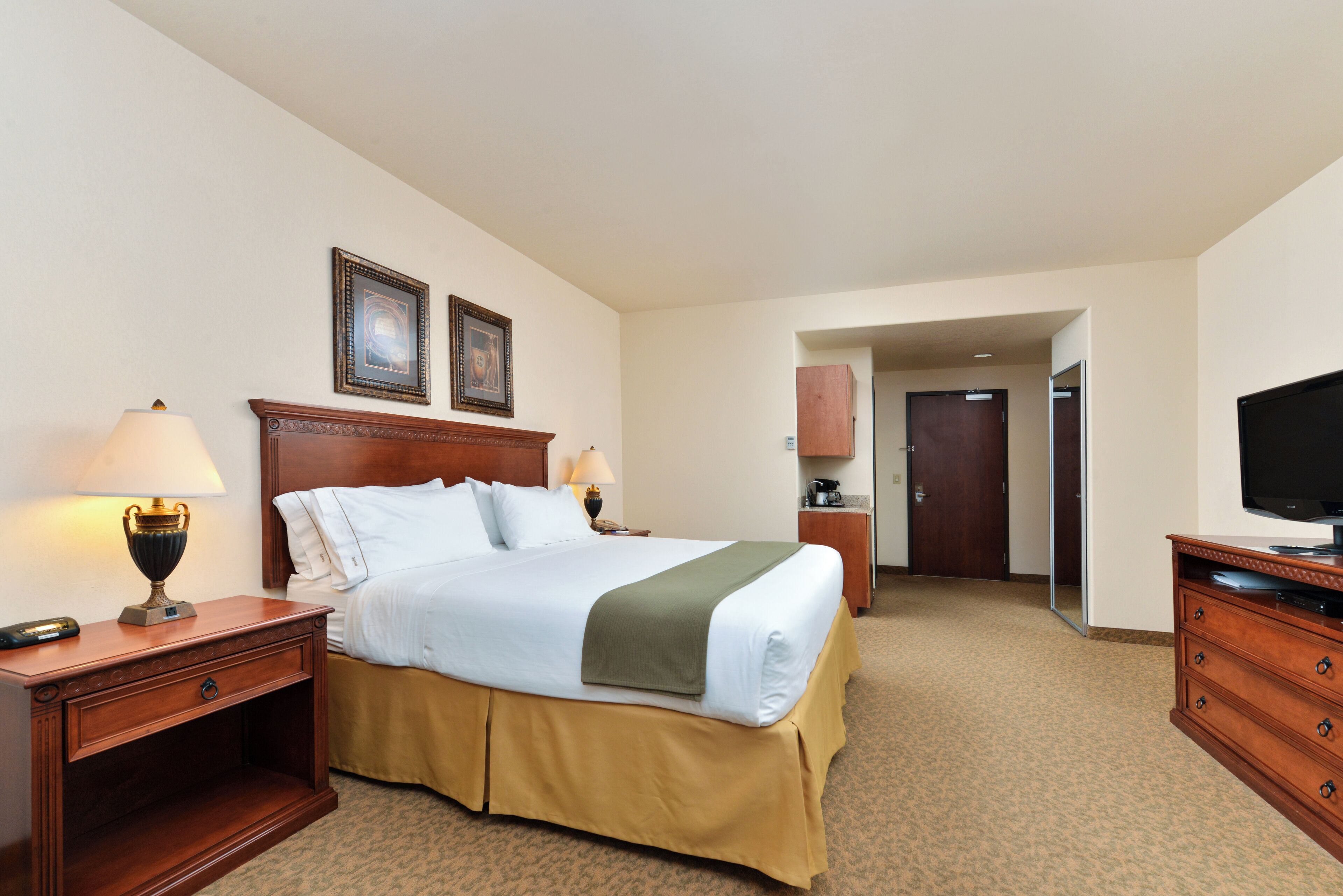 A hotel room with a large bed, two bedside tables with lamps, a television, and a wardrobe.