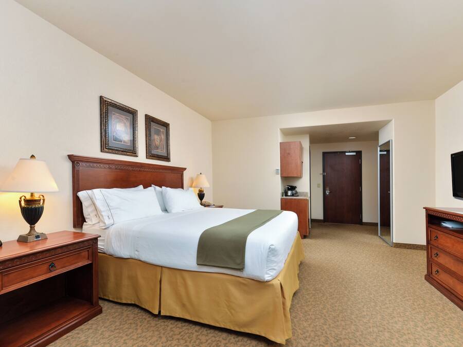 A hotel room with a large bed, two bedside tables with lamps, a television, and a wardrobe.