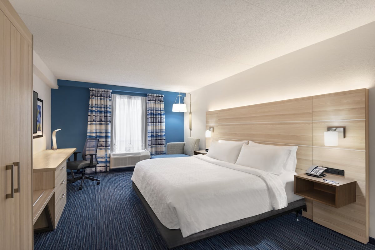 A hotel room with a bed, desk, chair, and a window with curtains.