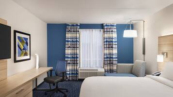 Quarto de hotel com cama, escrivaninha, cadeira, aparelho de ar condicionado e janela com cortinas.