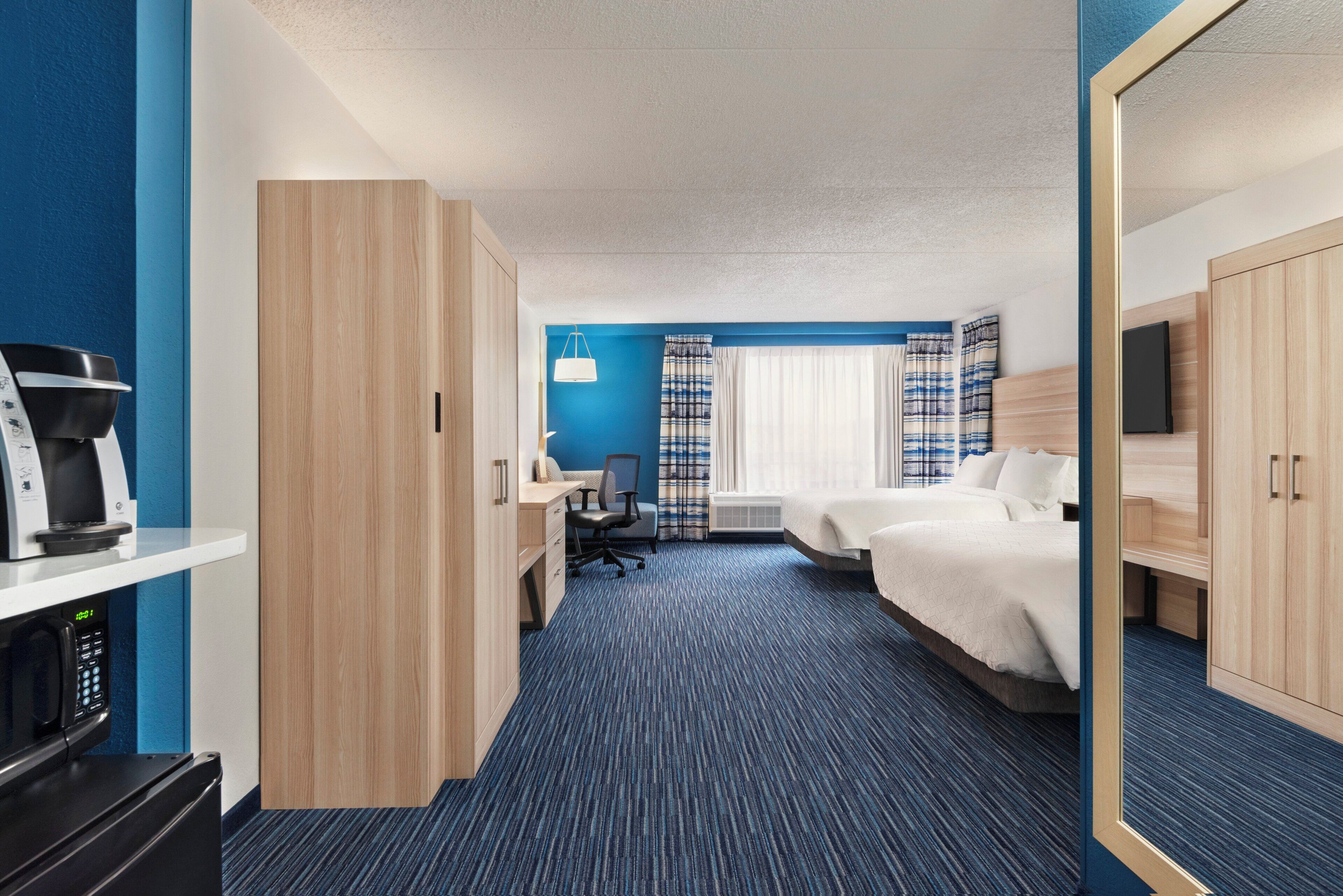 A hotel room with a desk, two beds, a TV, and a minibar.