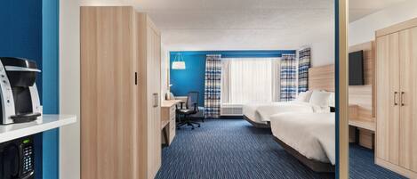 A hotel room with a desk, two beds, a TV, and a minibar.