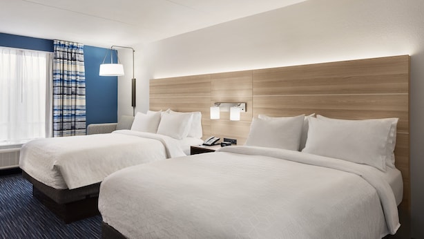 Een hotelkamer met twee bedden, een nachtkastje met een telefoon, een wandlamp en een raam met gordijnen.