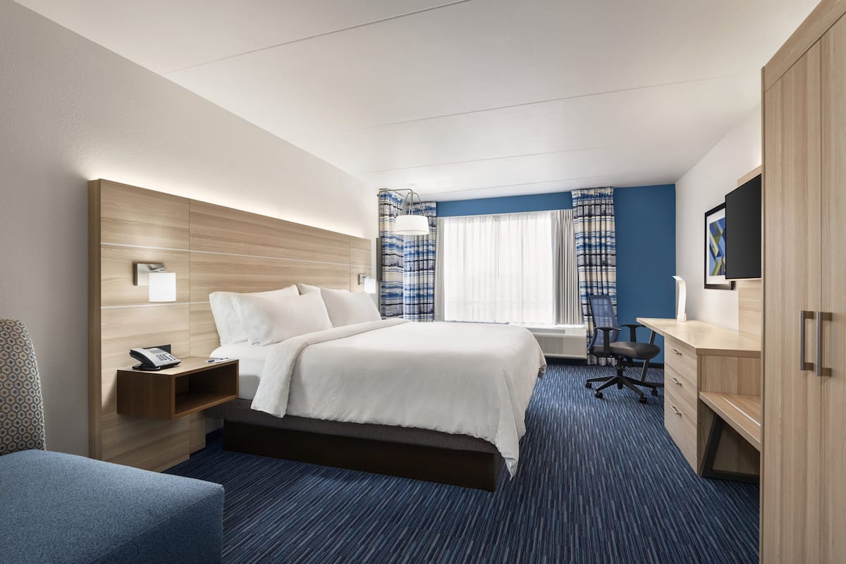 A hotel room with a bed, a desk, a chair, a TV, and a window with curtains.